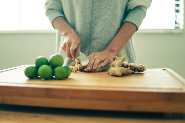 Woman chopping fresh ginger, next to a pile of limes on a wooden cutting board