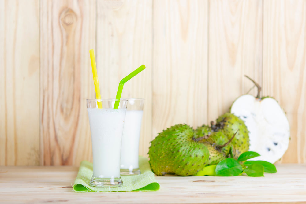 A glass of soursop drink beside whole and halved soursop fruit